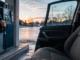 An empty passenger seat in a family car beside a gas pump at dawn, illustrating persistent U.S. energy inflation and pressure on household costs.