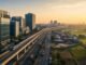 Modern Indian business district, elevated rail and logistics corridor beside agricultural fields at sunrise