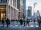 Commuters cross a city business district street as office towers, trucks and construction cranes illustrate the U.S. economy and a slowing hiring engine.