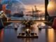 An empty diplomatic table overlooking a port, semiconductor wafer and mineral materials symbolising U.S.–China negotiations over trade, technology and critical minerals